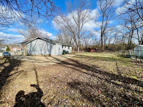 A person is taking a photo of a house with bare trees and a blue sky in the background.
