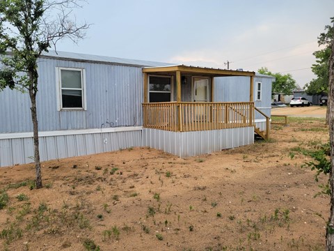 A blue house with a wooden deck and a tree in front.