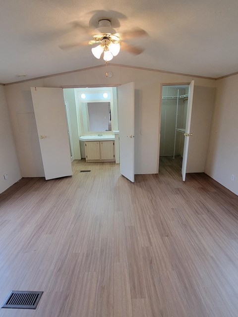 A room with a ceiling fan and light, hardwood floors, and a large mirror.