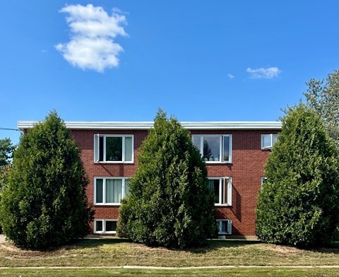A red brick building with white trim and windows is surrounded by green trees.