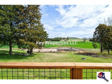 A fence with a view of a field and trees with Key Properties LLC written on it.
