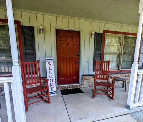 A porch with a red door and two chairs.