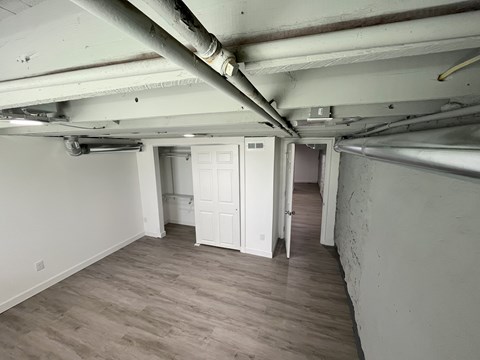 A room with a white door and a white wall with a pipe running along the ceiling.