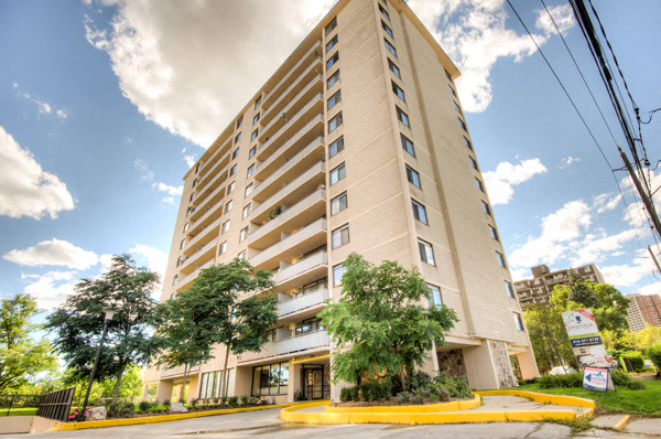 A tall beige apartment building with a yellow entrance and trees in front.