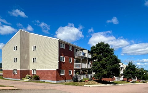 A large apartment building with a red brick facade and a balcony on the second floor.