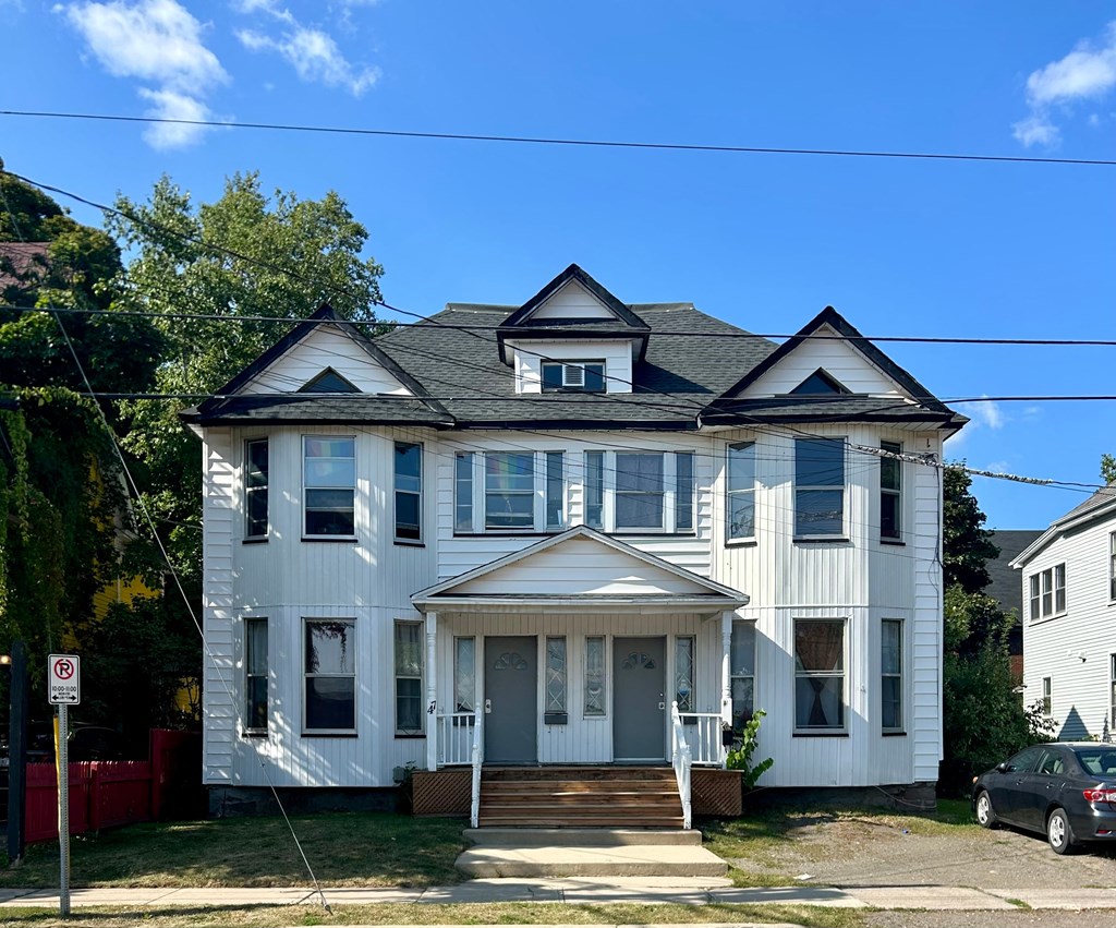 A white two-story house with a black roof and a car parked in front.