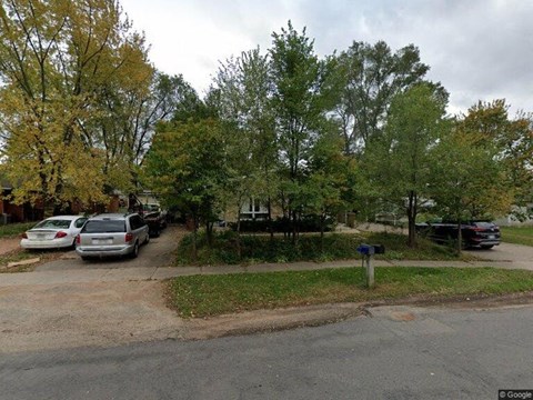 A street view with cars parked on the side and trees in the background.
