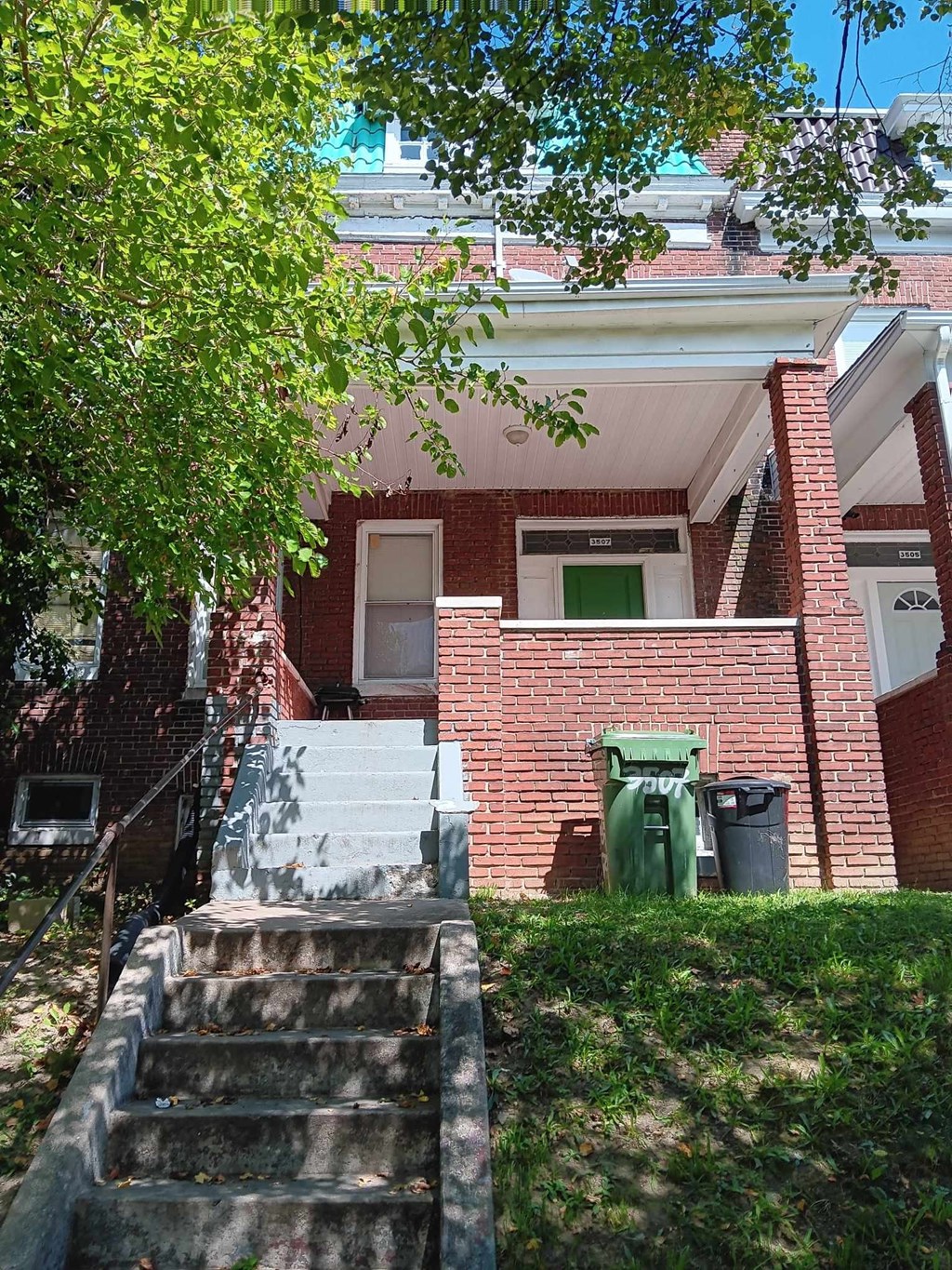 A red brick house with a green trash can and a tree in front.