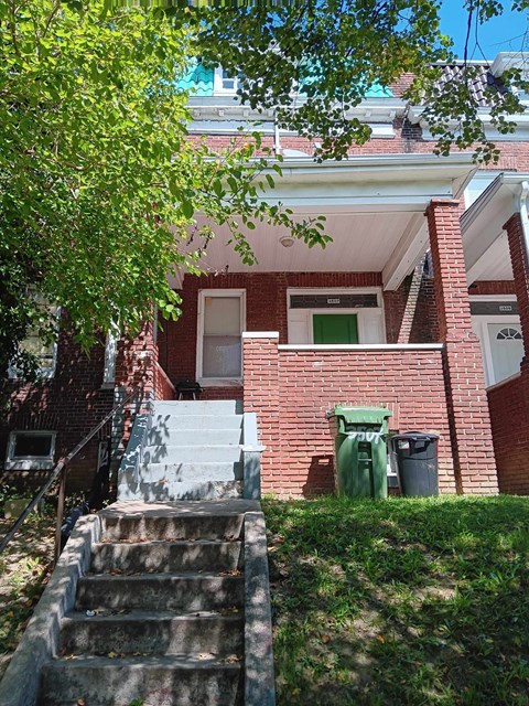 A red brick house with a green trash can and a tree in front.
