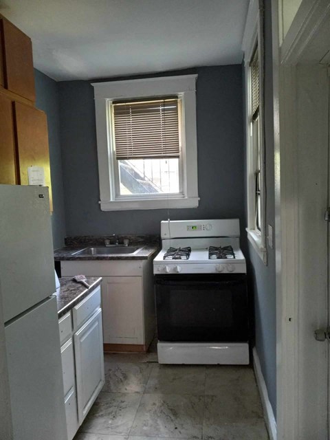 A kitchen with a white fridge, white oven, and a window with blinds.