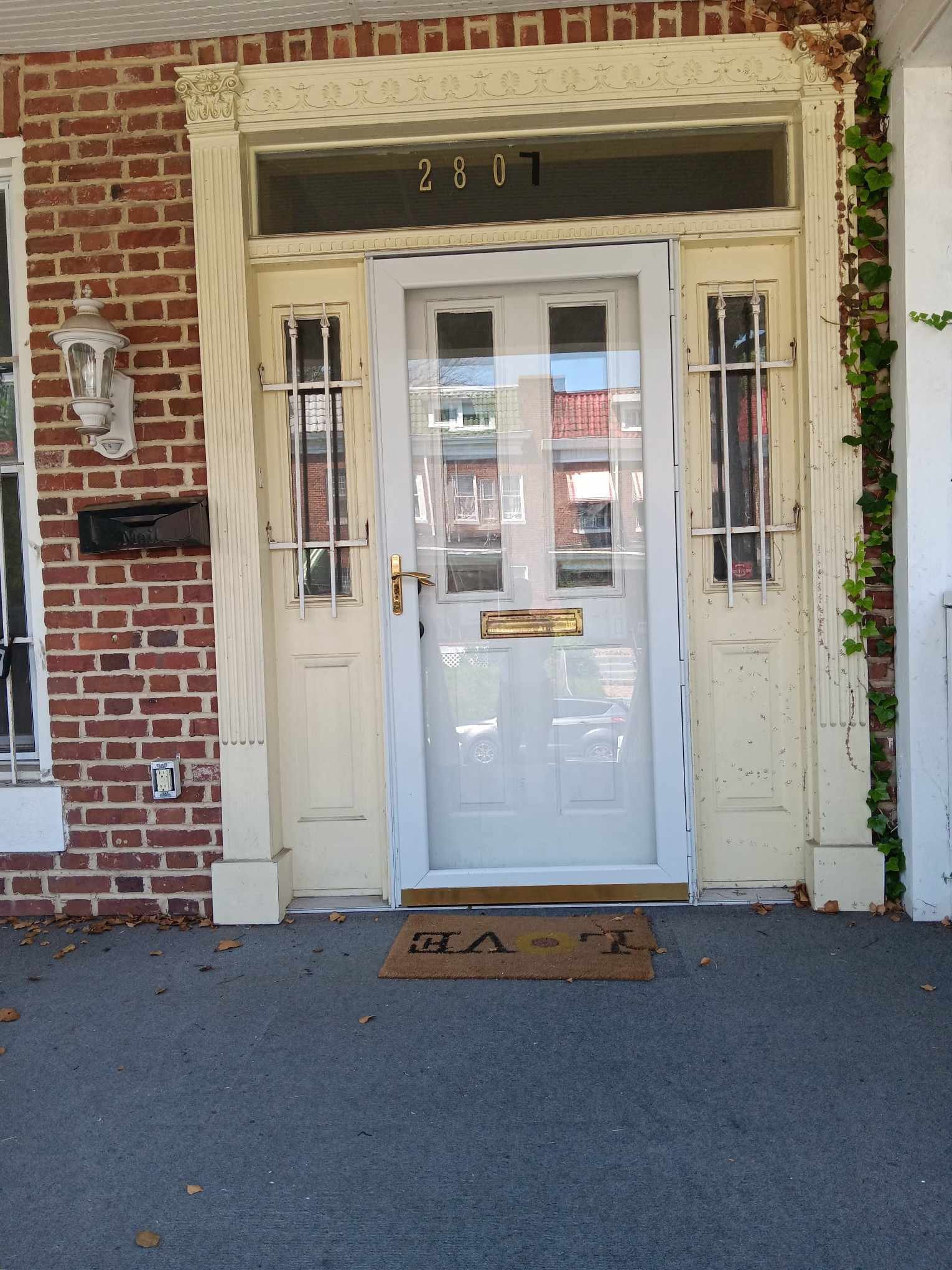 A white door with a glass window and a mailbox on a brick wall.