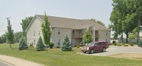 A red car is parked in front of a two-story house.