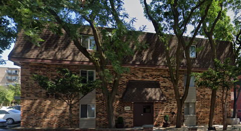 A brick building with a brown door and windows surrounded by trees.