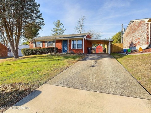 A red brick house with a gravel driveway in front.
