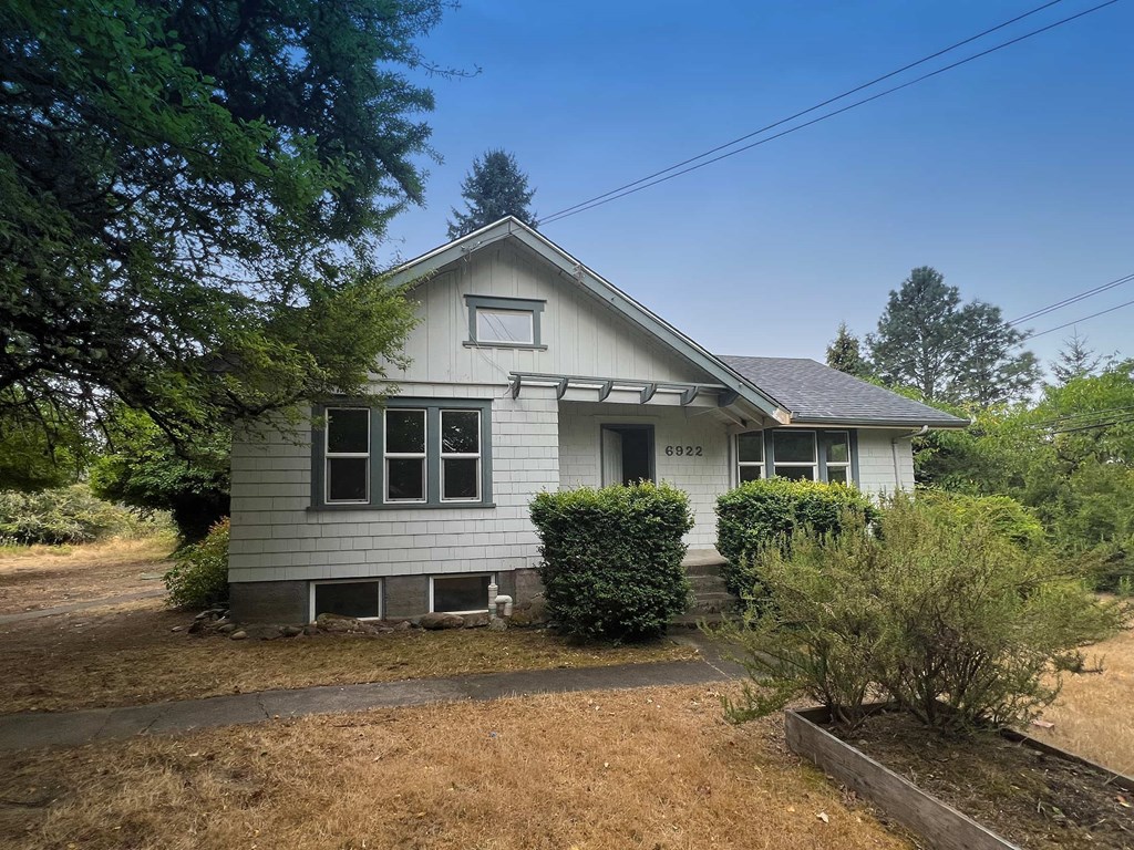 A house with a grey roof and white walls is surrounded by greenery.