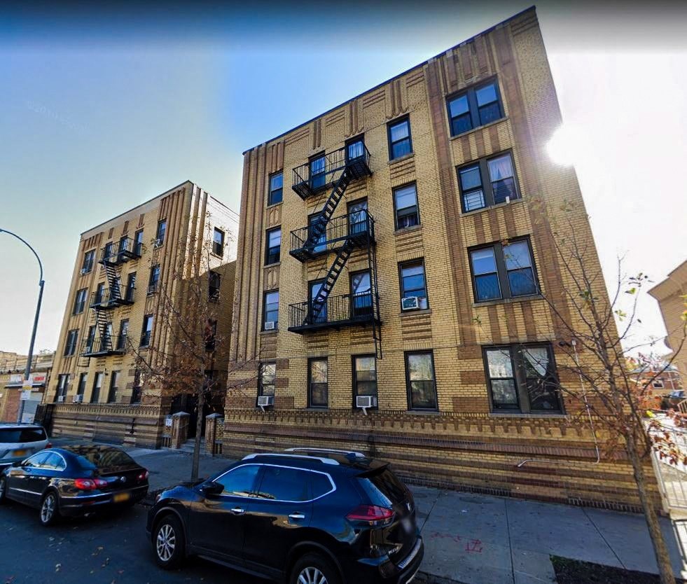 A black car is parked on the sidewalk in front of a brown building with a fire escape.