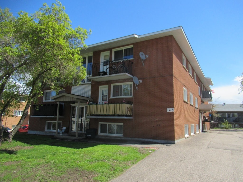 A red brick apartment building with a balcony and a tree in front.