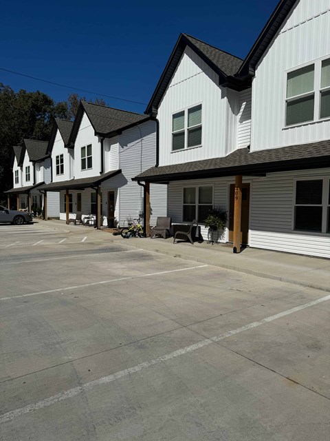 A parking lot in front of a white building with black roofs.