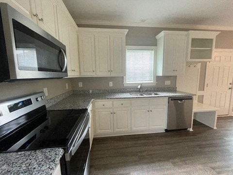 A kitchen with white cabinets and a black microwave.