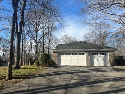 A two-car garage is situated in a driveway with a tree-lined background.