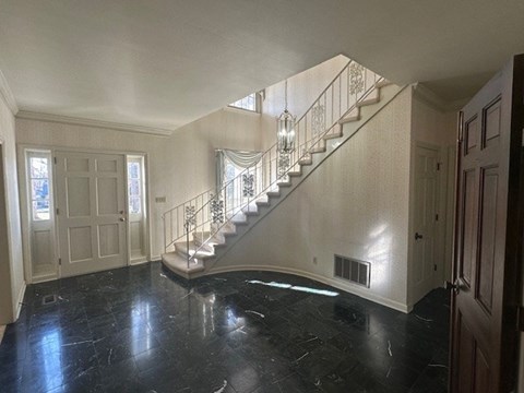 A spacious foyer with a marble floor and a staircase with a metal railing.