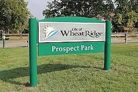 A sign for Wheat Ridge Prospect Park is displayed in a grassy area.