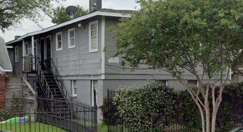 A grey house with a black fence and a tree in front.