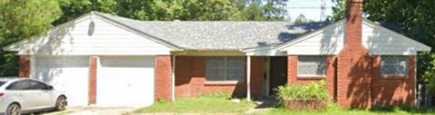 A white car is parked in front of a red brick house.