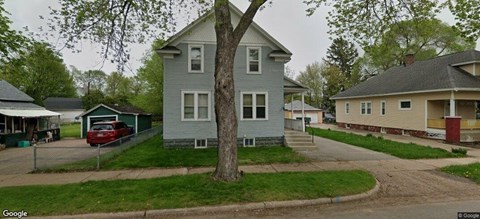 A tree in front of a grey house.