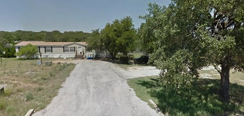 A gravel road leads to a house in a wooded area.