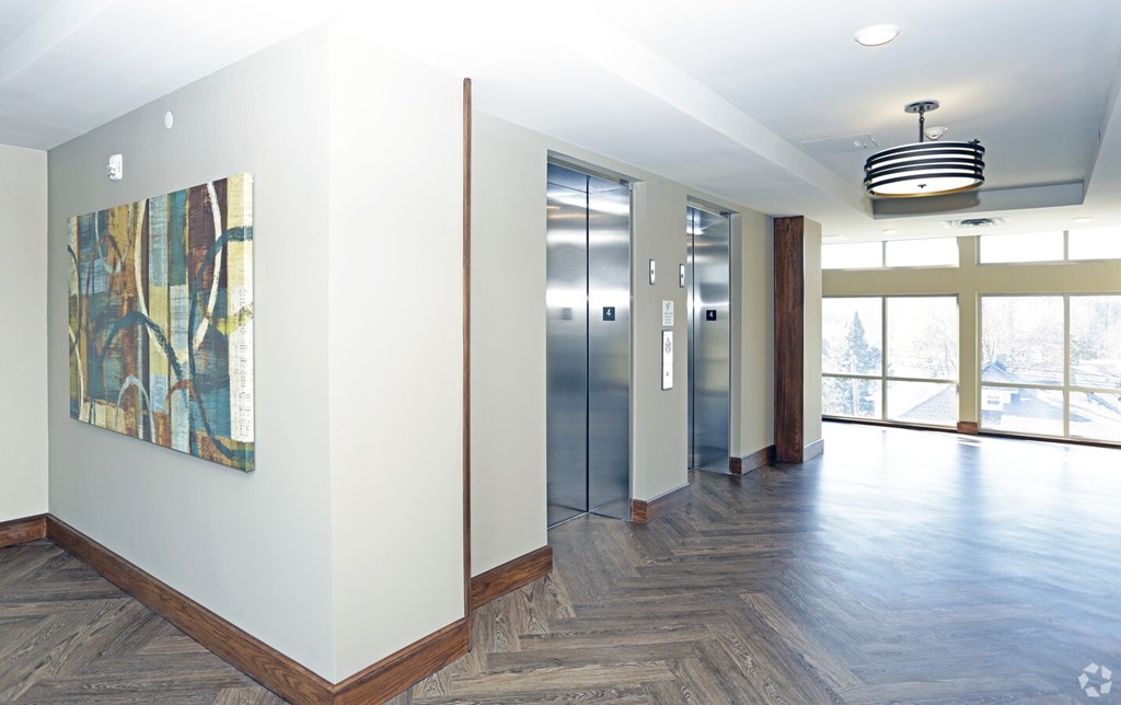 A hallway with wood floors, a ceiling light, and a painting on the wall.