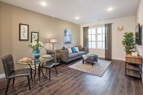 A living room with a glass table and chairs, a grey sofa, a blue armchair, and a wooden coffee table.