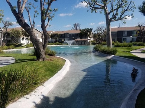 A small waterfall in a garden with a building in the background.