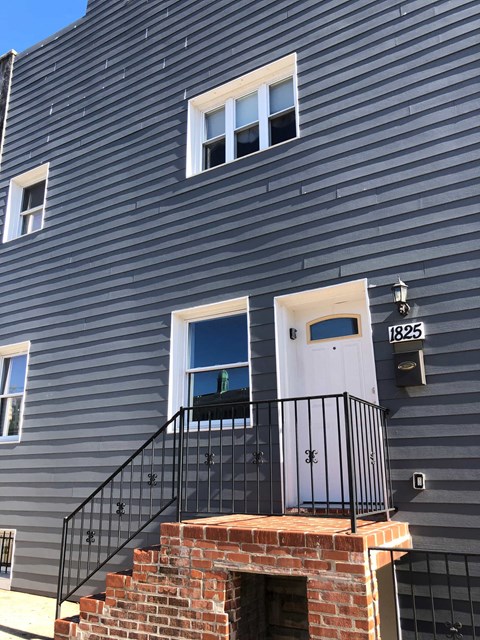 A grey building with a black railing and a white door.