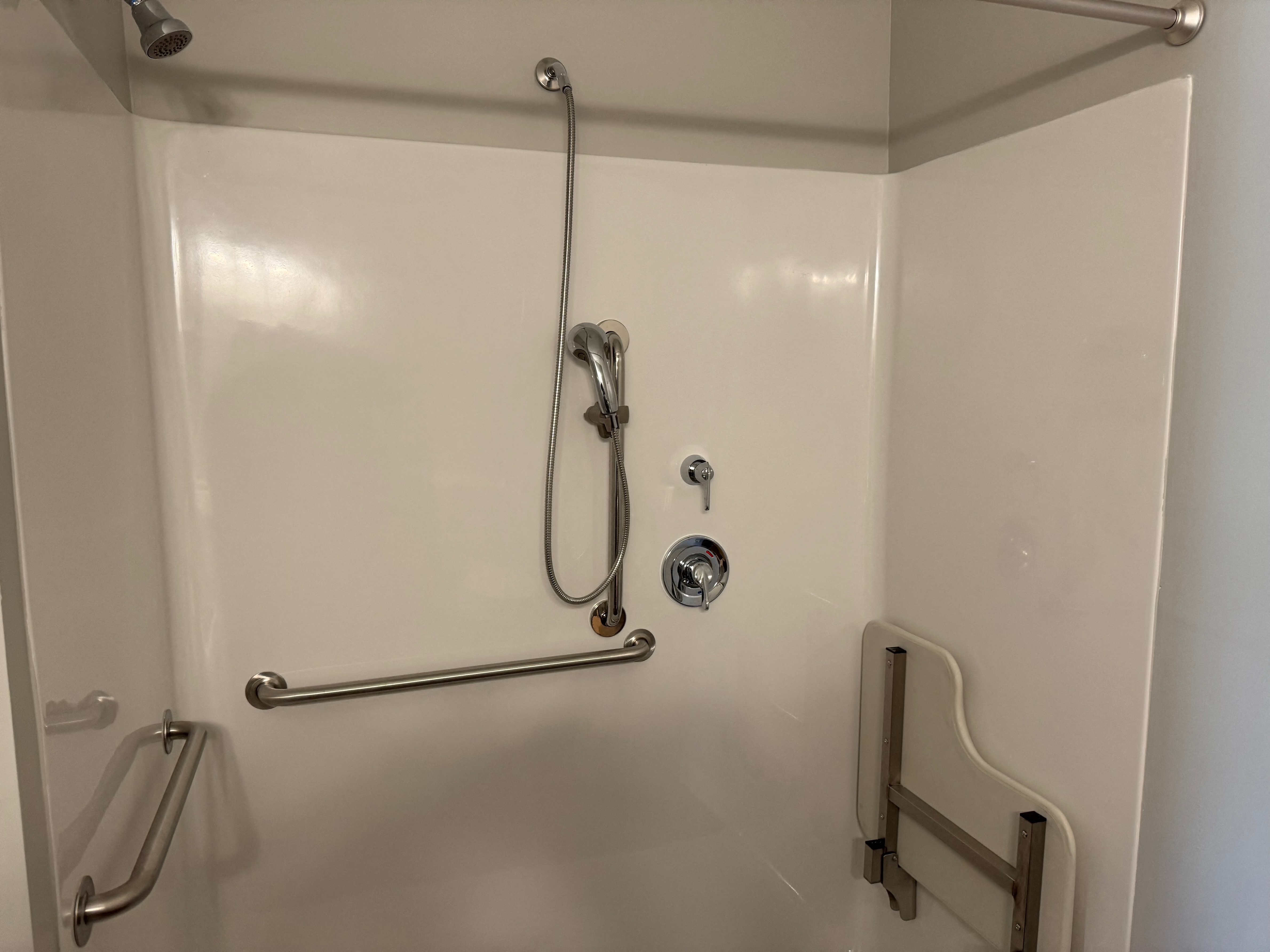 A white shower stall with a shower head and hand held shower.