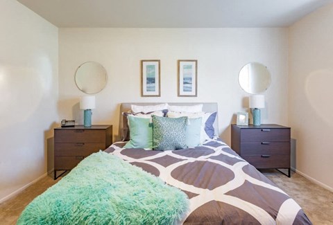 A bedroom with a bed, two nightstands, and two round mirrors on the wall.