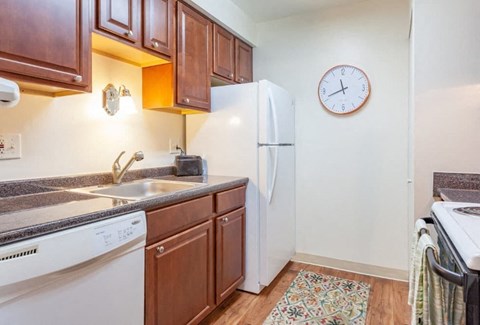 A small kitchen with a white fridge and a clock on the wall.