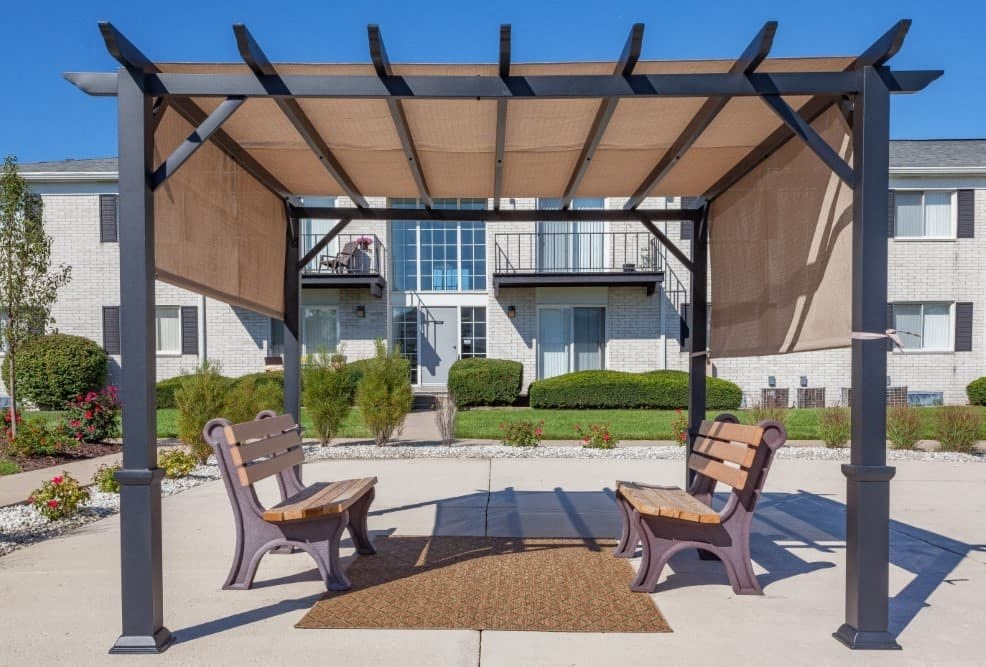 A wooden bench is situated under a wooden pergola.