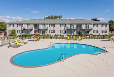 A large swimming pool in front of a building with sun loungers around it.