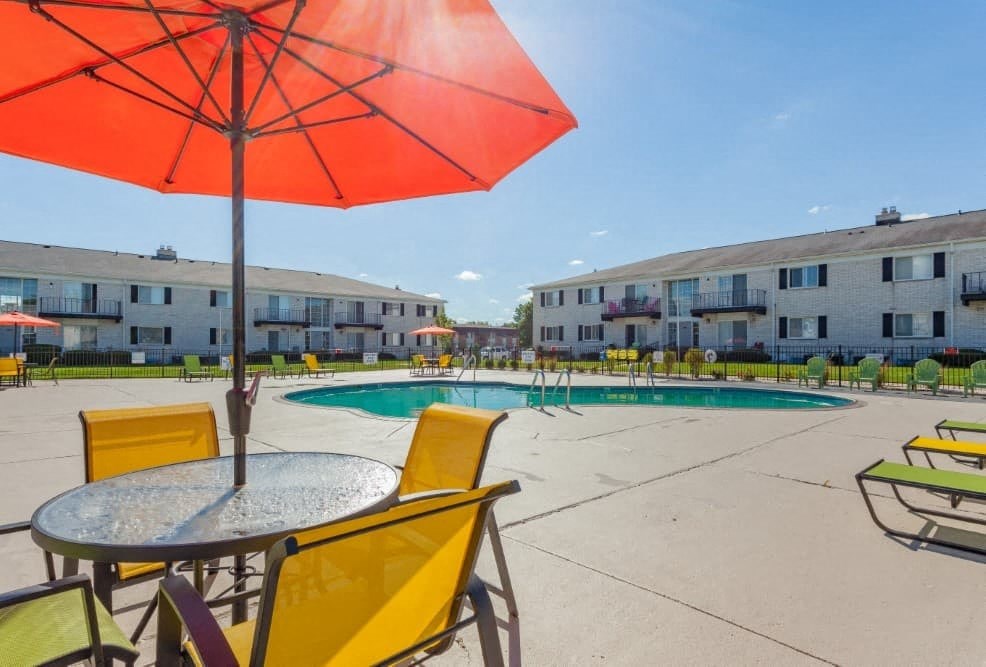 A red umbrella is in the foreground of a sunny outdoor pool area.