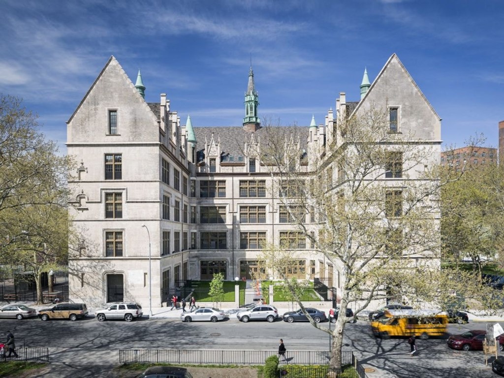 A large, historic building with a green spire stands in front of a parking lot.