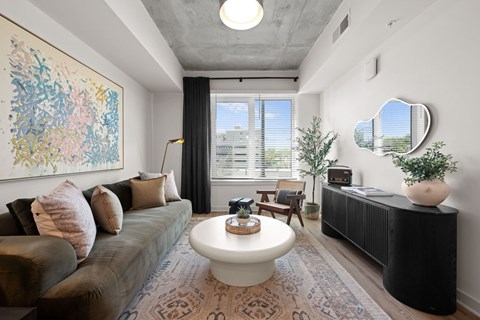 A living room with a brown couch, a white coffee table, and a large painting on the wall.
