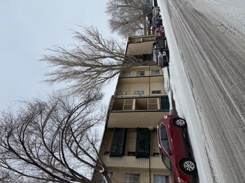 A red car is stuck in a snow bank in front of a building.