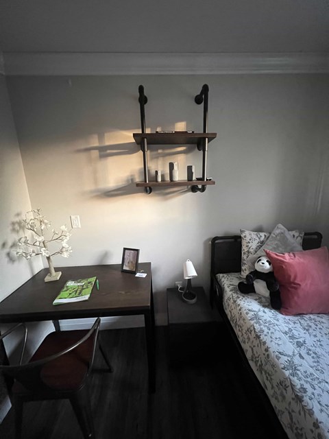 A bedroom with a bed, desk, chair, and shelf.