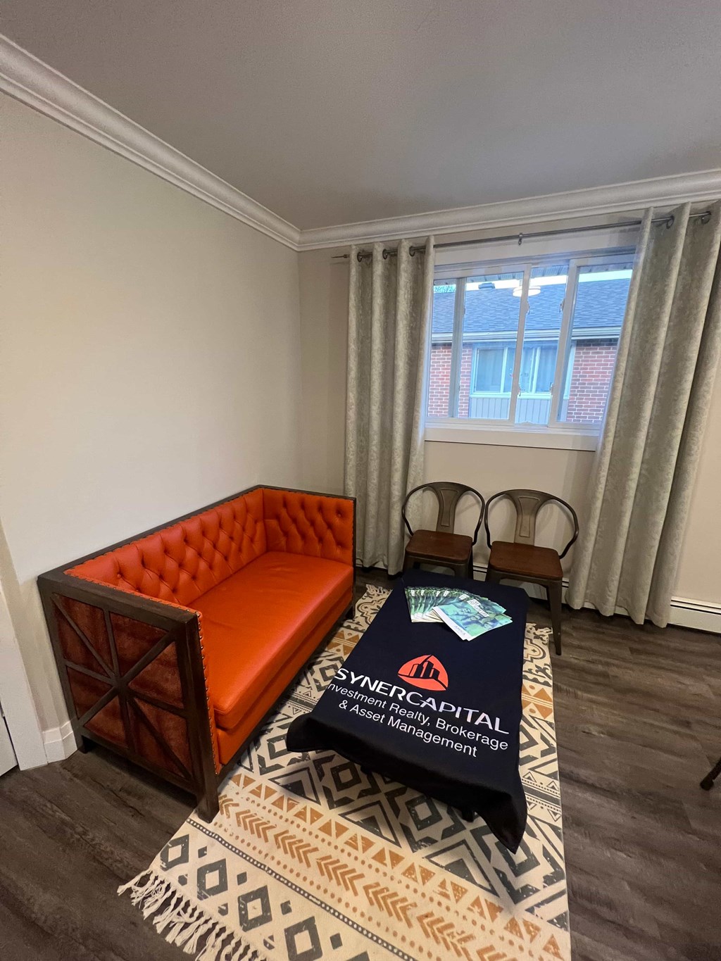 A room with a sofa, chairs and a table with a Synchron Capital tablecloth on it.
