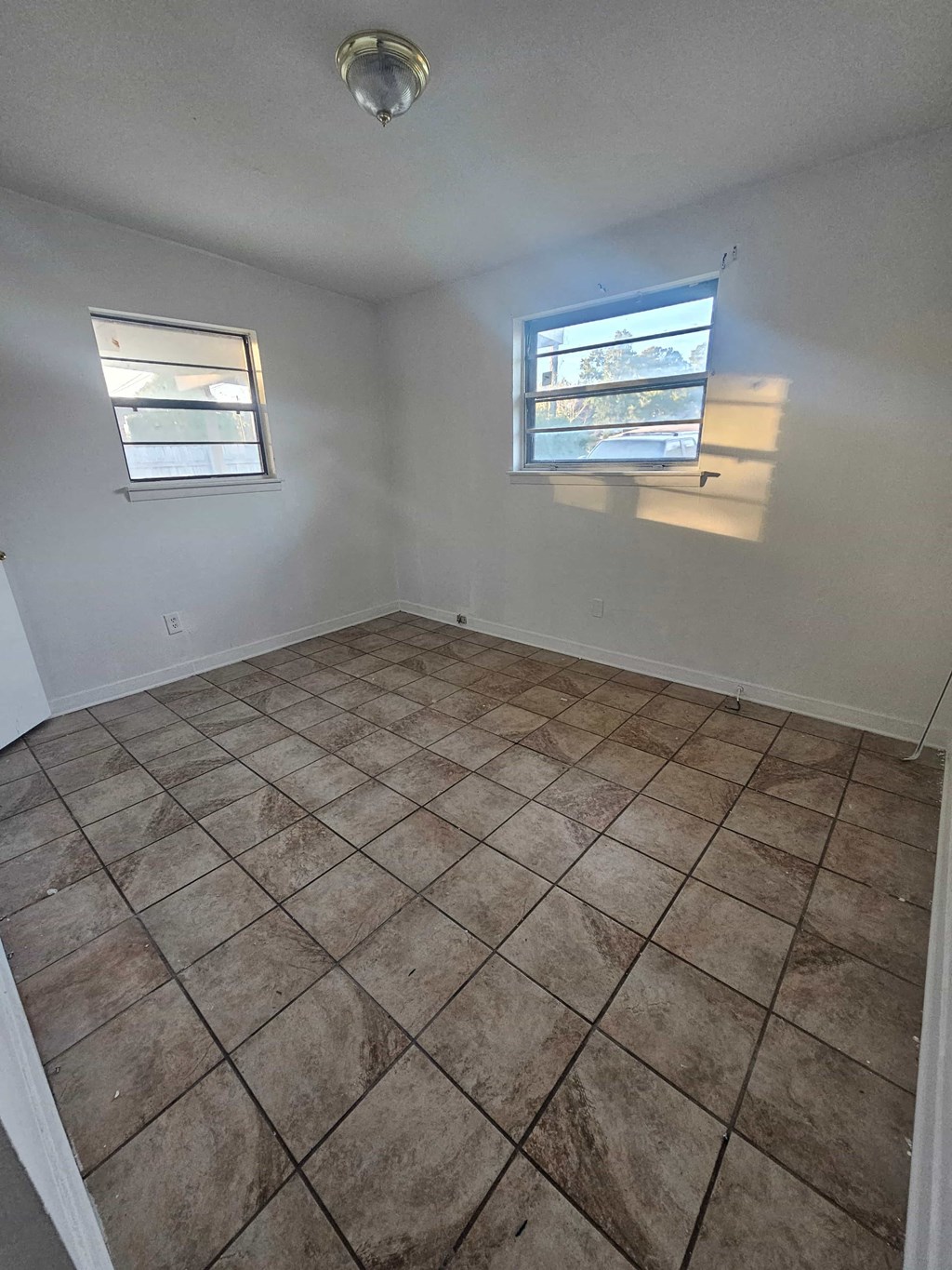 A room with tile flooring and two windows.