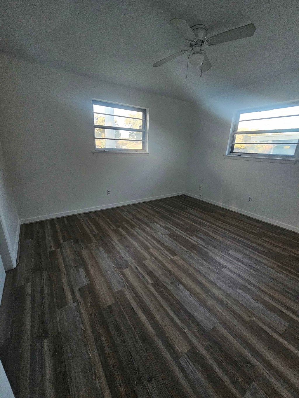 A room with wooden flooring and two windows.