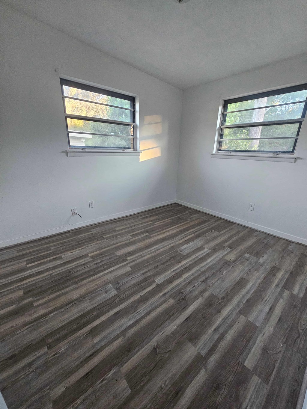 A room with wooden flooring and two windows.