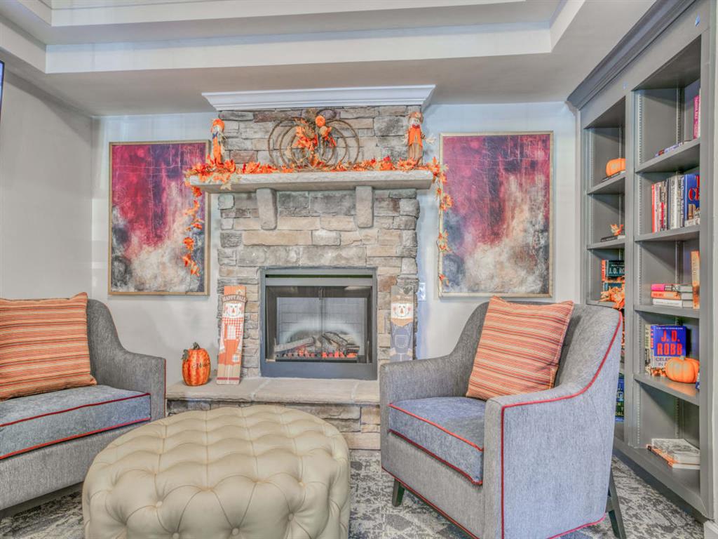 A living room with a grey couch, a grey ottoman, and a fireplace with a painting above it.
