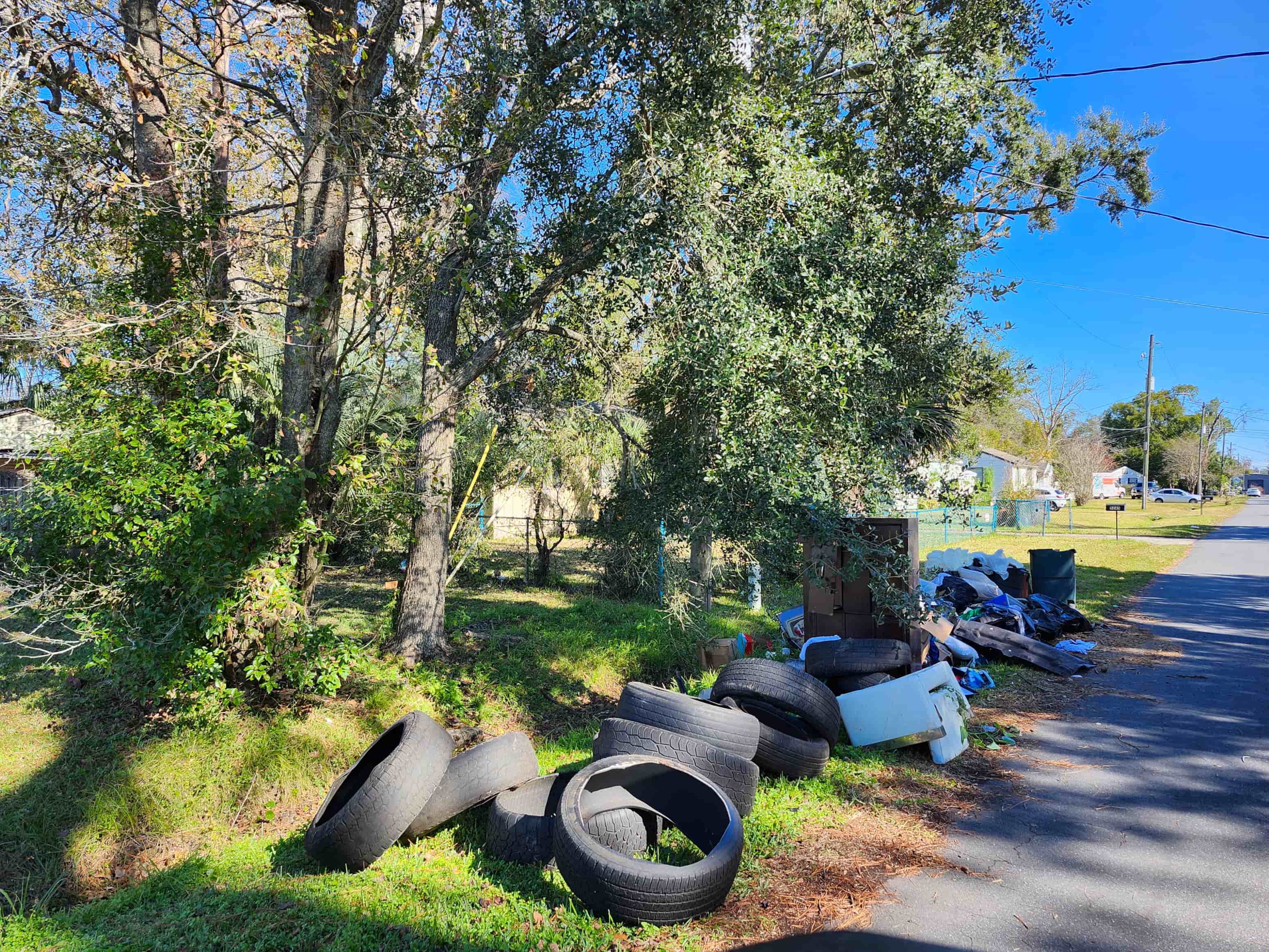 A pile of old tires are on the grass by the road.